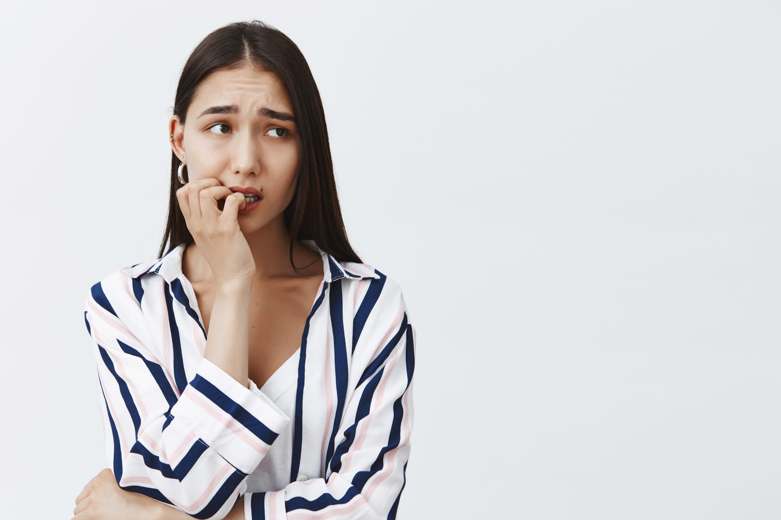 horizontal-shot-anxious-good-looking-female-student-striped-blouse-biting-fingernail-nervously-frowning-looking-aside-being-scared-consequences-standing-gray-wall (1)